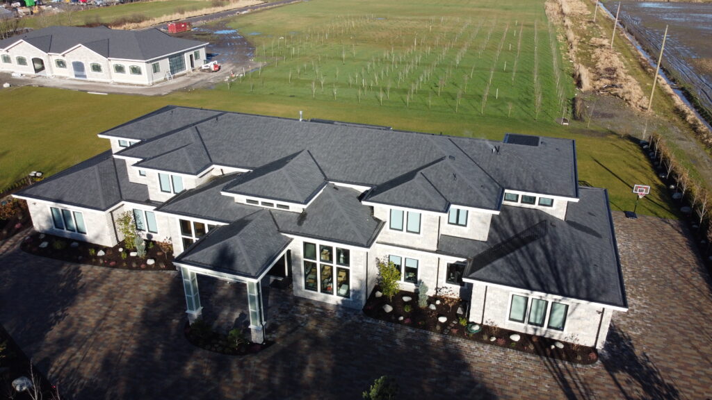 Aerial view of a large, modern house at 14791 Westminister Hwy with a gray roof and white walls, surrounded by a patterned driveway and green fields.