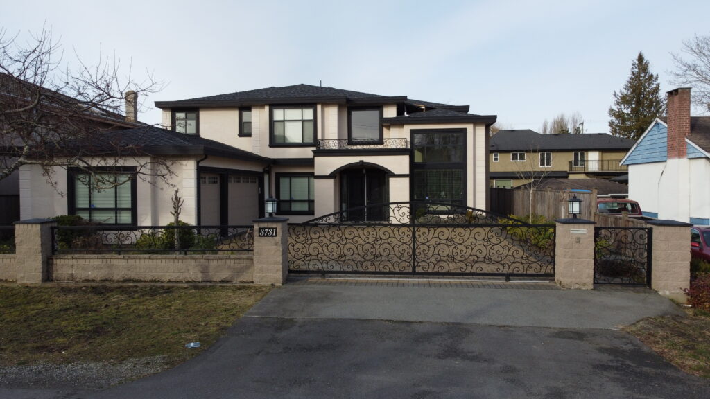 A large two-story house at 3731 Barmond Drive with a black wrought iron gate, beige walls, and a gray roof, surrounded by leafless trees and green lawn.