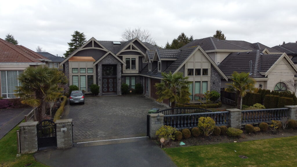 Aerial view of a large, modern property listing at 5651 Colville Rd, featuring a gray roof, multiple gables, and a paved driveway with a white car parked.
