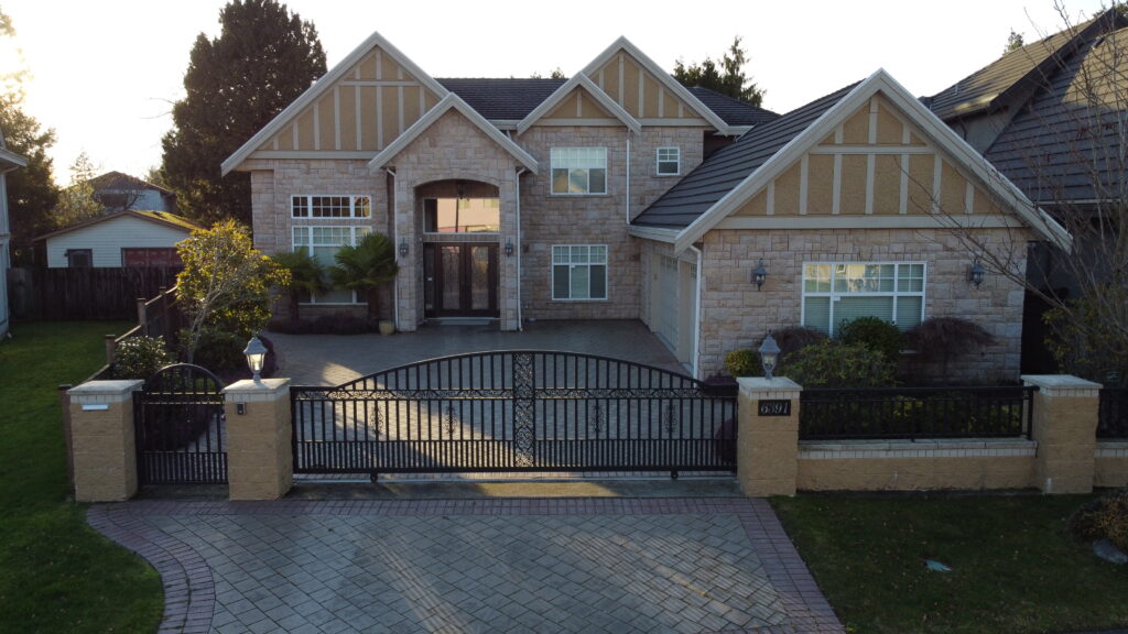 Aerial view of a large two-story house on Clematis Drive with a stone facade, gabled roofs, and a gated driveway, set in a suburban area with green lawns.