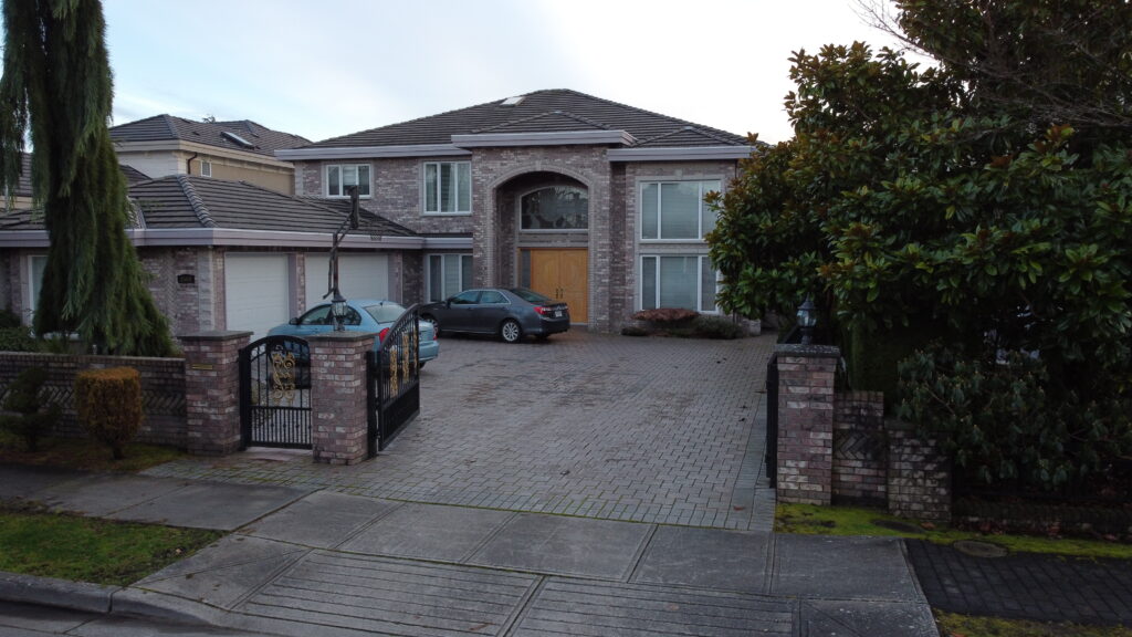 Aerial view of a large house on Chatterton Road with a tile roof, featuring a driveway with two parked cars, surrounded by landscaped greenery and a metal gate.