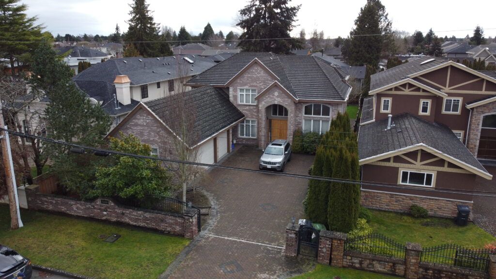Aerial view of a suburban neighborhood at 7400 Lucas Road featuring a large house with a grey roof and a white car parked in the driveway, surrounded by similar homes and bare trees.