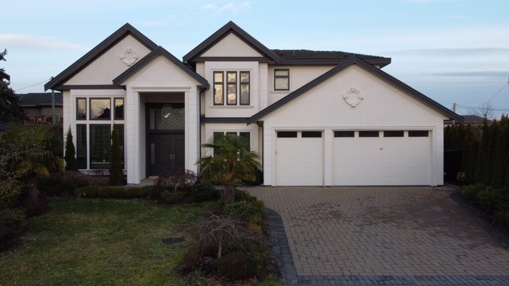 Modern two-story house in Chelsea Place with a large garage and a paved driveway, surrounded by manicured landscaping under a clear sky at dusk.