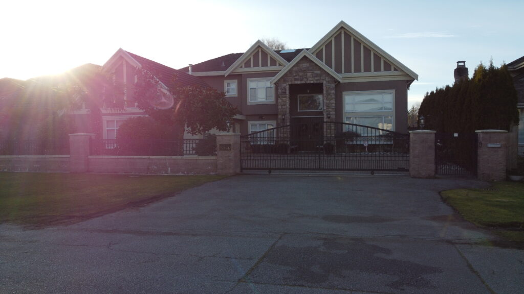 Large two-story house at 8540 Bairdnore Crescent with a prominent gable, large windows, and a gated driveway, captured in sunlight.