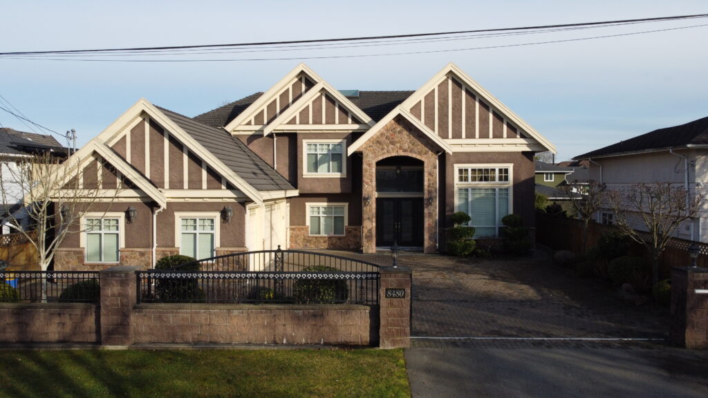 Large suburban two-story home with a brown and beige facade, gabled roofs, and a fenced front yard under a clear sky at 8580 Farihurst Road.