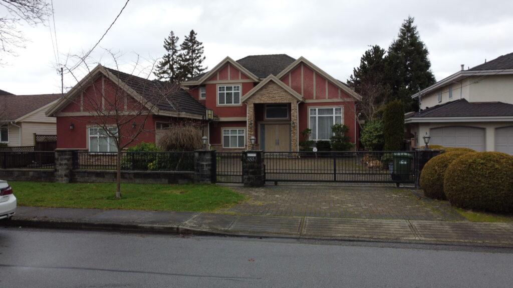 A red and beige suburban house at 8851 Wheeler Road with a gabled roof, fronted by a black wrought-iron fence, on an overcast day.