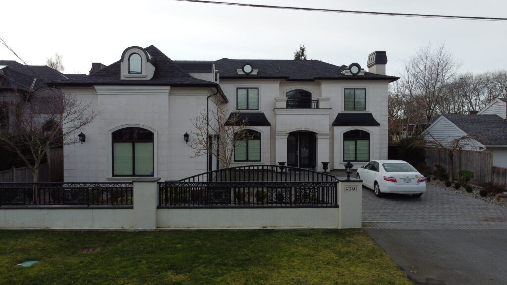A large, two-story house located at 9390 Piermond Road with white walls and black trim, featuring multiple roofs and a gated front yard with a white sedan parked outside.